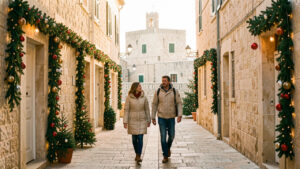 Vue hivernale de La Valette à Malte, avec des ruelles en pierre dorée décorées de verdure et de lumières chaleureuses, tandis qu’une femme et un homme en vestes légères se promènent sous la douce lumière de décembre.